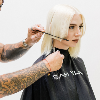 stylist with comb cutting hair of woman with blonde bob