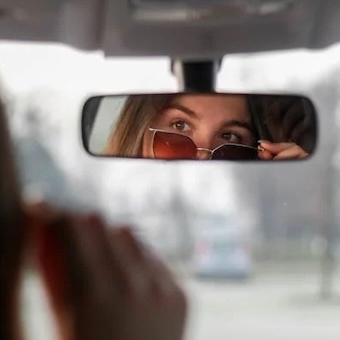 Woman looking into rear view mirror wearing sunglasses