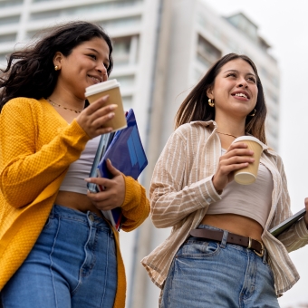 Two female students walking outstide holding books and coffee