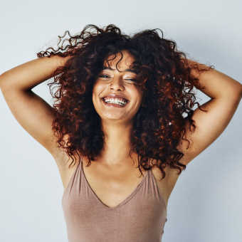 Woman with brown curly hair smiling and using her hands to play with her hair