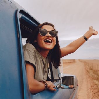 Smiling woman wearing sunglasses waves her hand outside a blue vehicle window