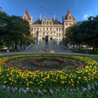 New York state capitol building with trees on either side and flowers in front of the steps