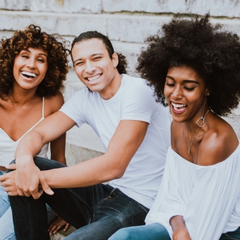 Three friends laughing on a sidewalk against a brick wall