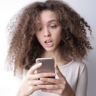 Woman with curly hair with shocked expression while looking at her cell phone